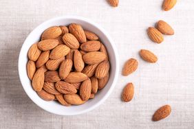 raw almonds in a white bowl and some on linen fabric