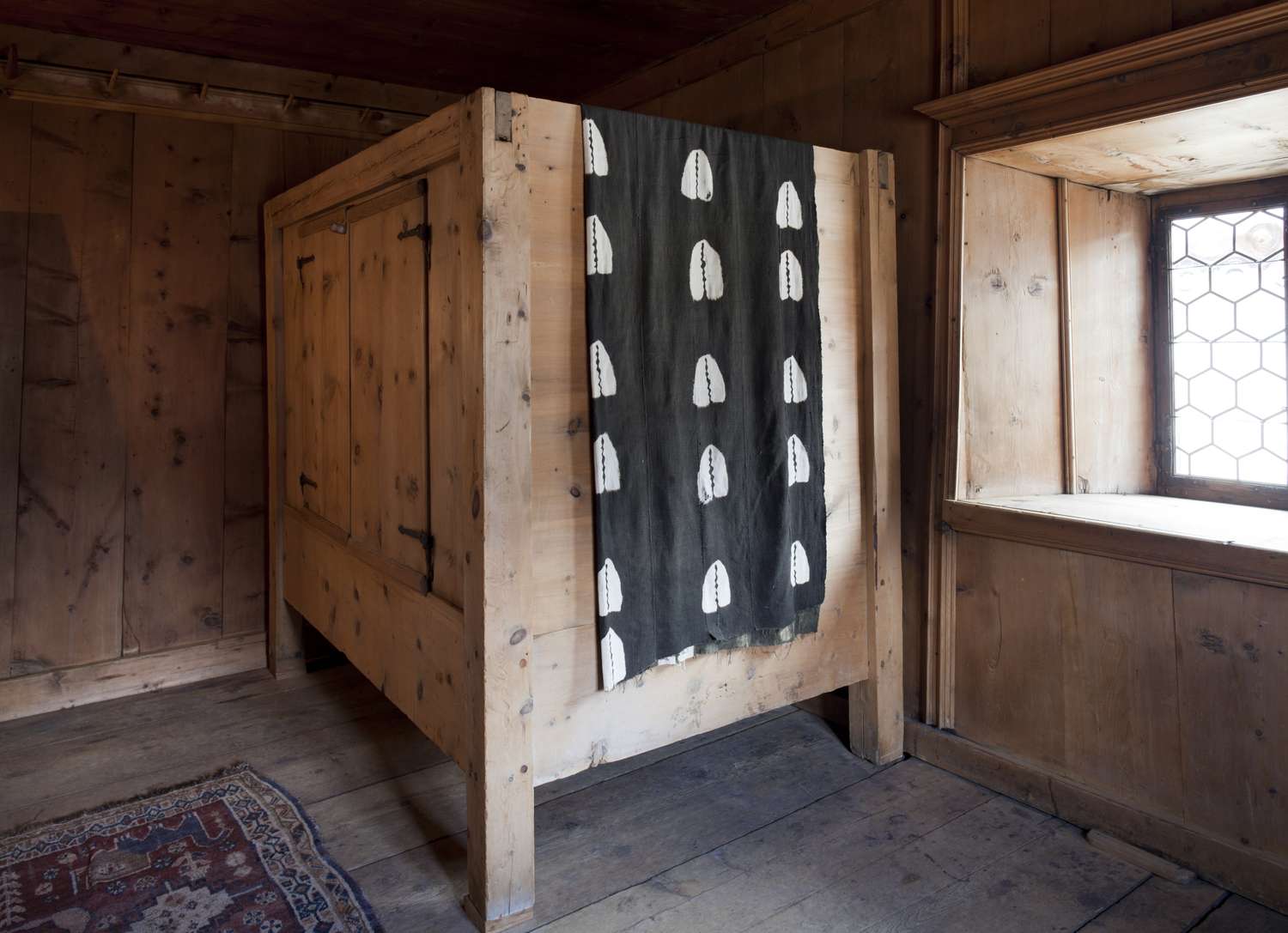 A wooden enclosed bed with a patterned curtain in a rustic interior with wooden walls and flooring