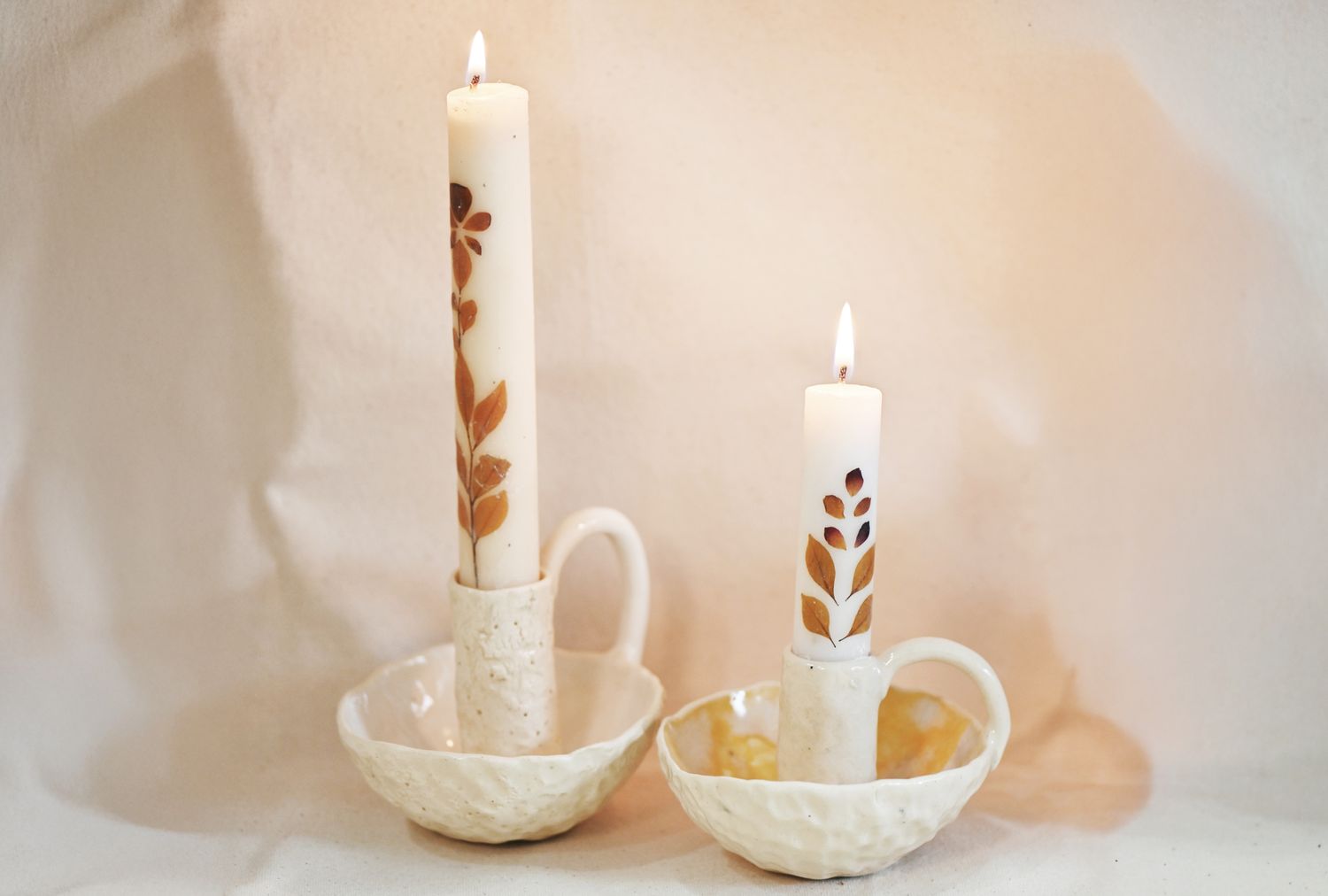 Two candles in ceramic candle holders featuring leaf patterns on the candles