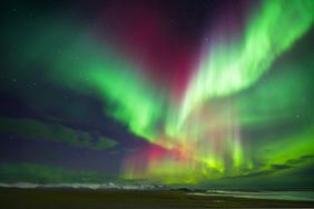 Northern lights display over a landscape with mountains and a body of water