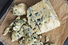 A block of blue cheese on parchment paper with crumbled pieces surrounding it