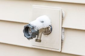 A wallmounted outdoor water spigot with some snow on it