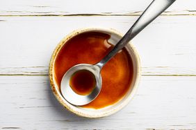 A small bowl of Worcestershire sauce with a spoon on a wooden surface