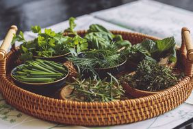 A wicker tray with fresh green herbs in small bowls on a table