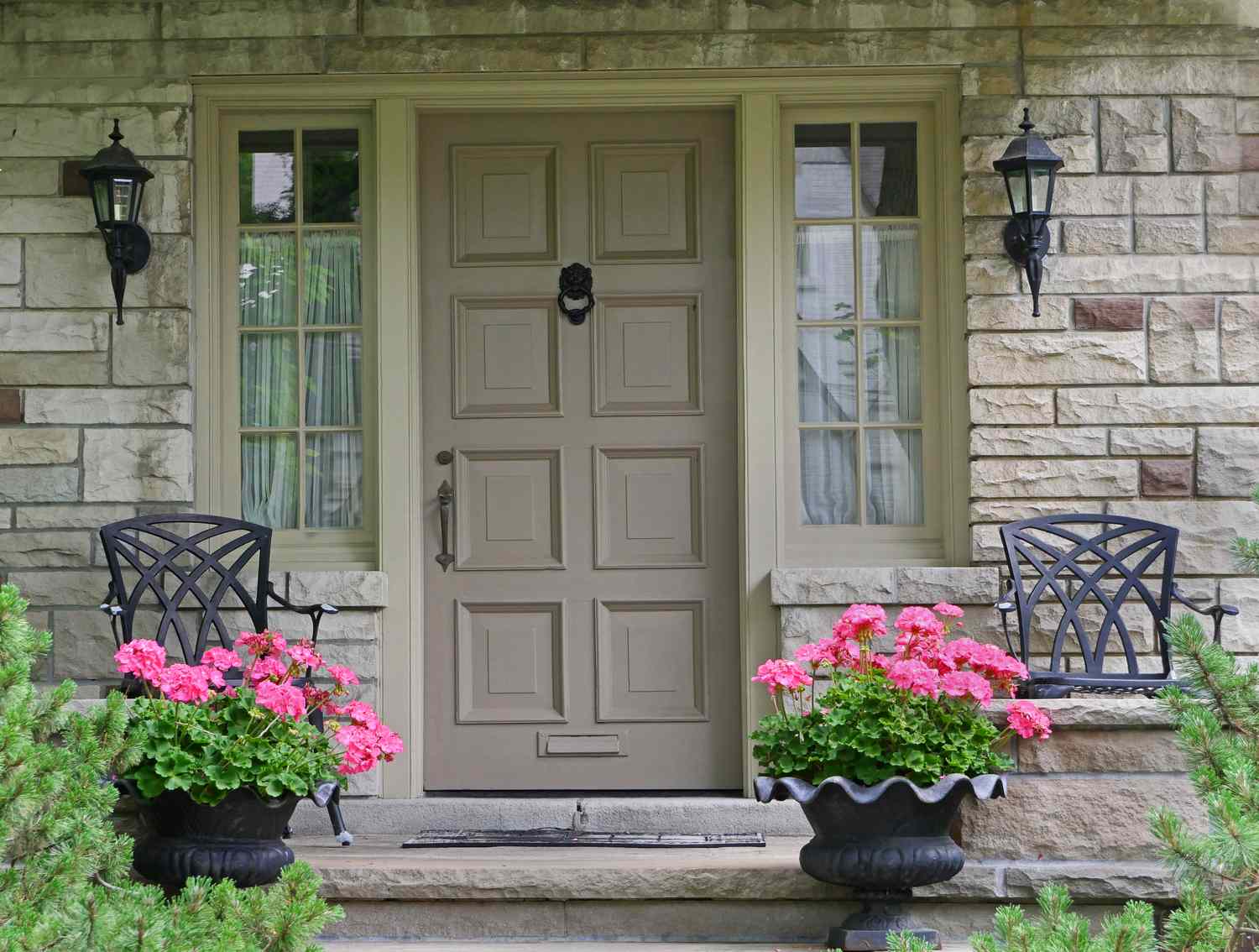 A front door with decorative planters and chairs on either side on a porch