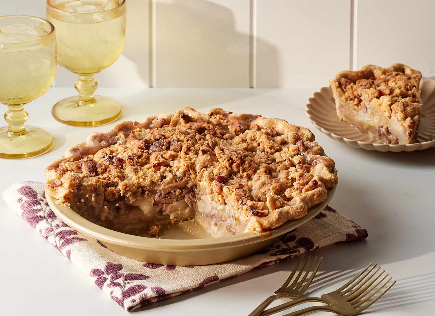 apple pie with piece removed, forks and drinks in background