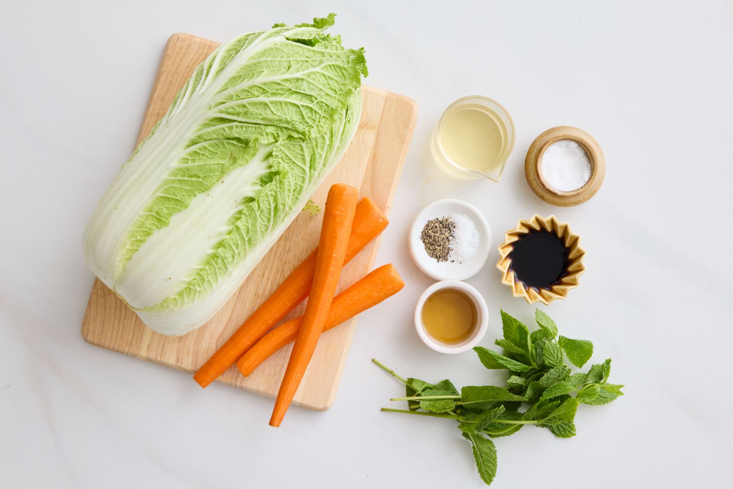 Ingredients for napa cabbage slaw including napa cabbage carrots and various seasonings on a cutting board and table