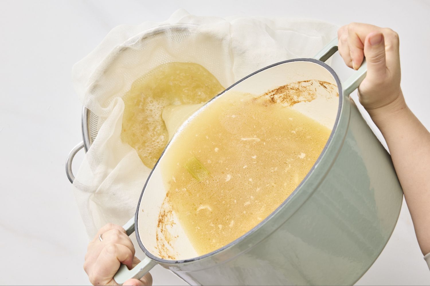 Straining chicken stock through a mesh sieve lined with cheesecloth