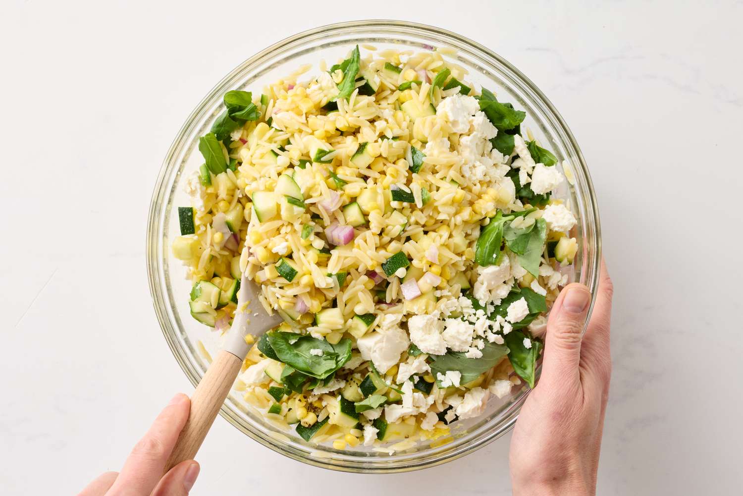 Bowl of corn and zucchini orzo salad being stirred with a spoon