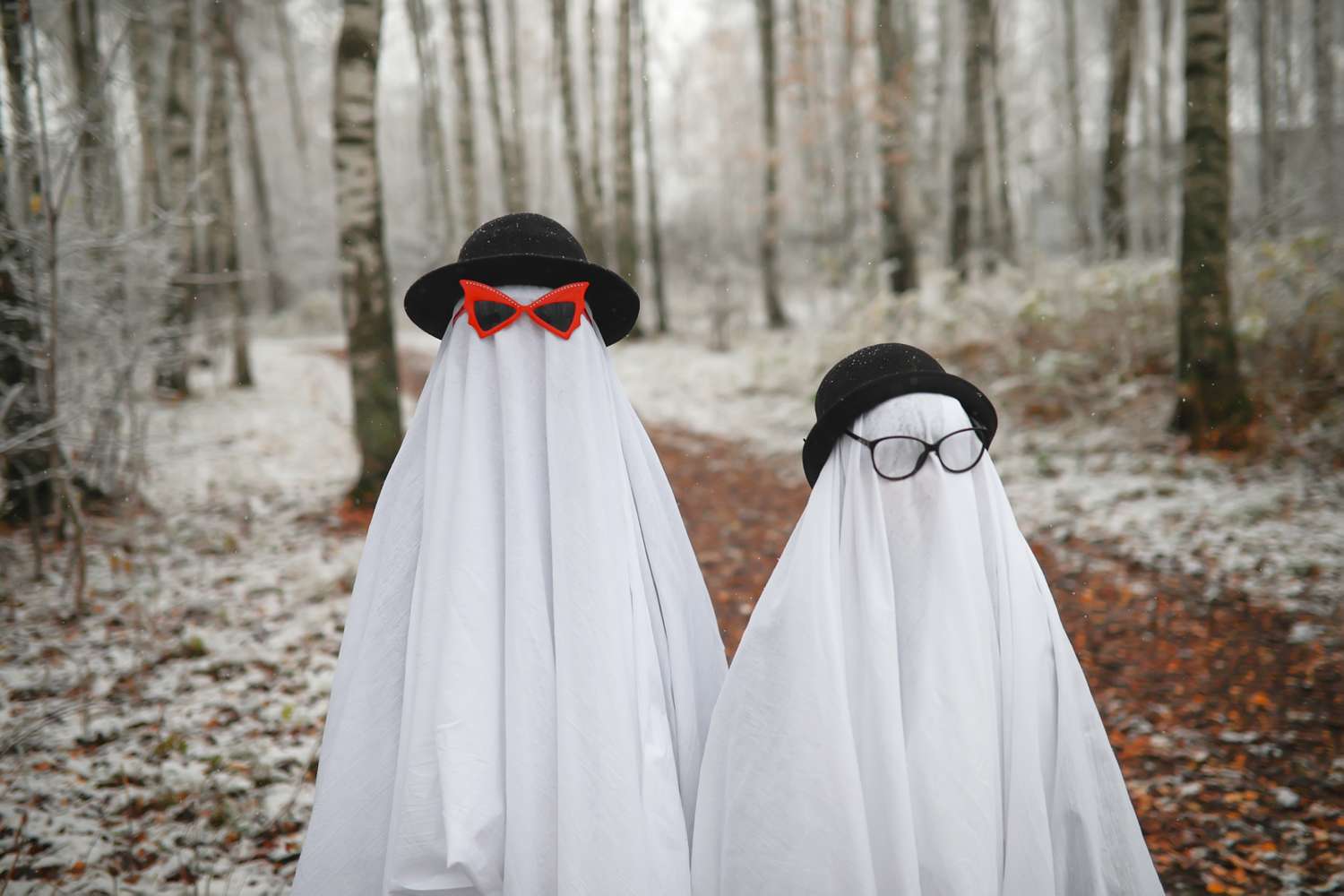 Two figures dressed as ghosts wearing hats and glasses standing on a forest path