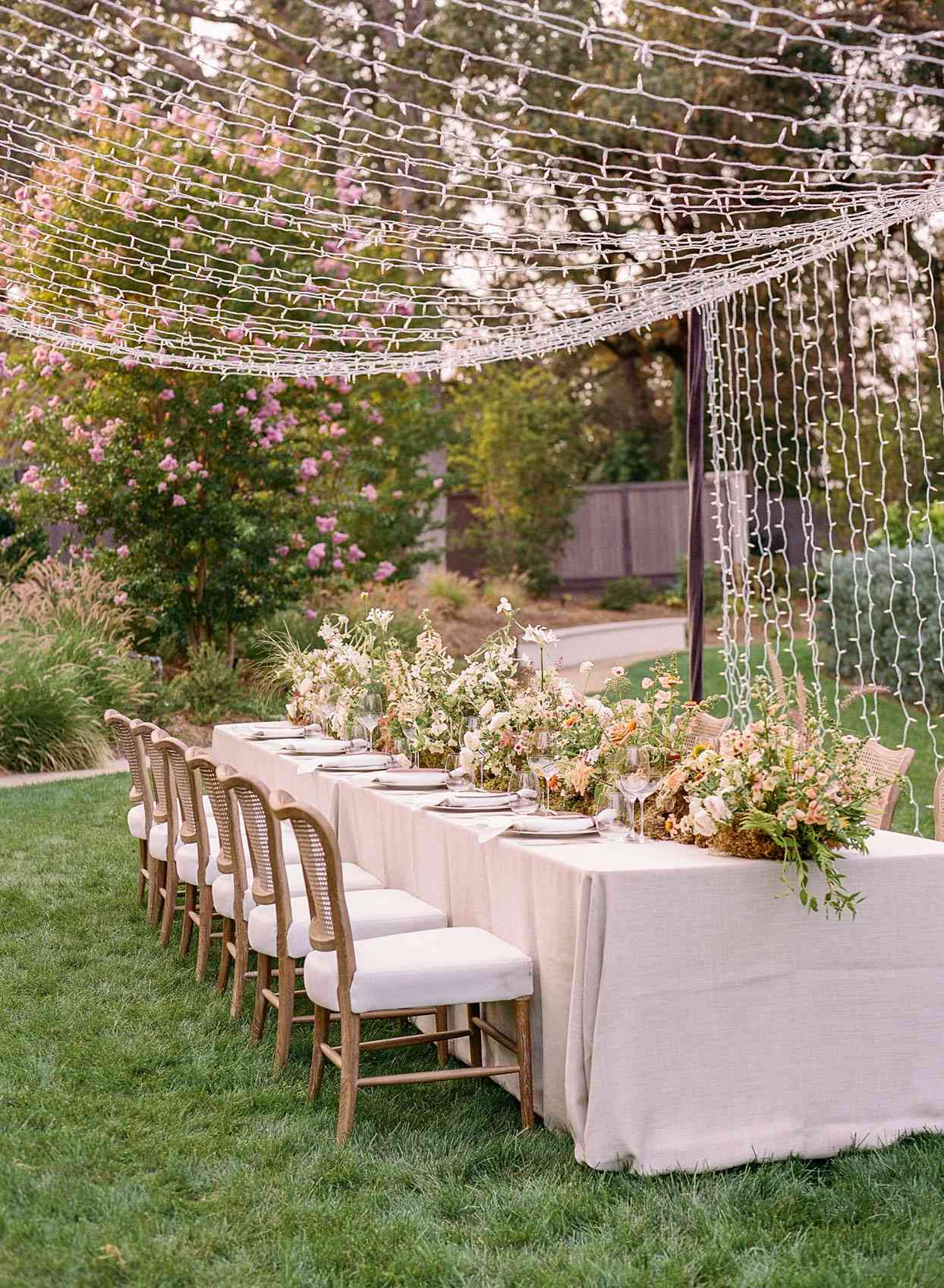 wedding reception table set up in grass with string lights above