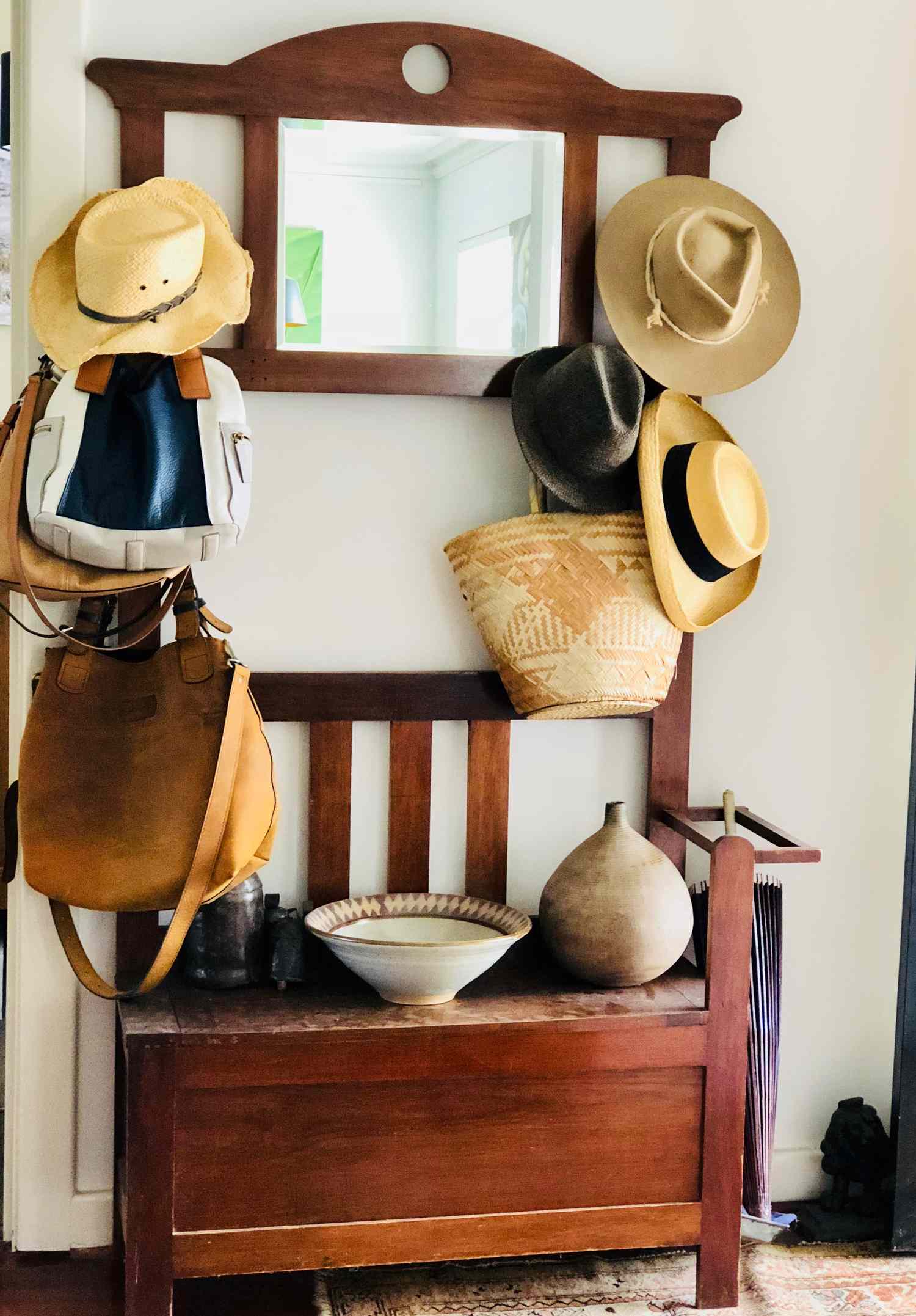 Wooden entryway bench with hats bags and woven baskets hanging on hooks with additional decorative items placed on the seat