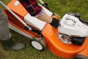 A person operating an orange lawnmower on grass