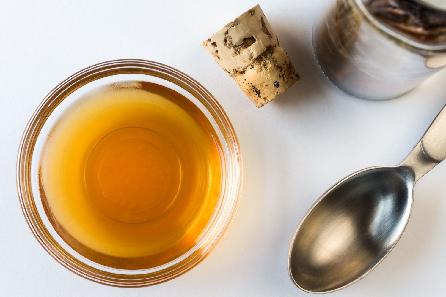 Bowl of sherry a metal spoon and a cork on a white background