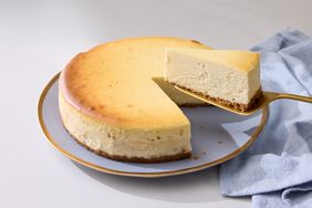 A cheesecake with a slice being lifted on a serving utensil placed on a plate with a blue cloth beside it