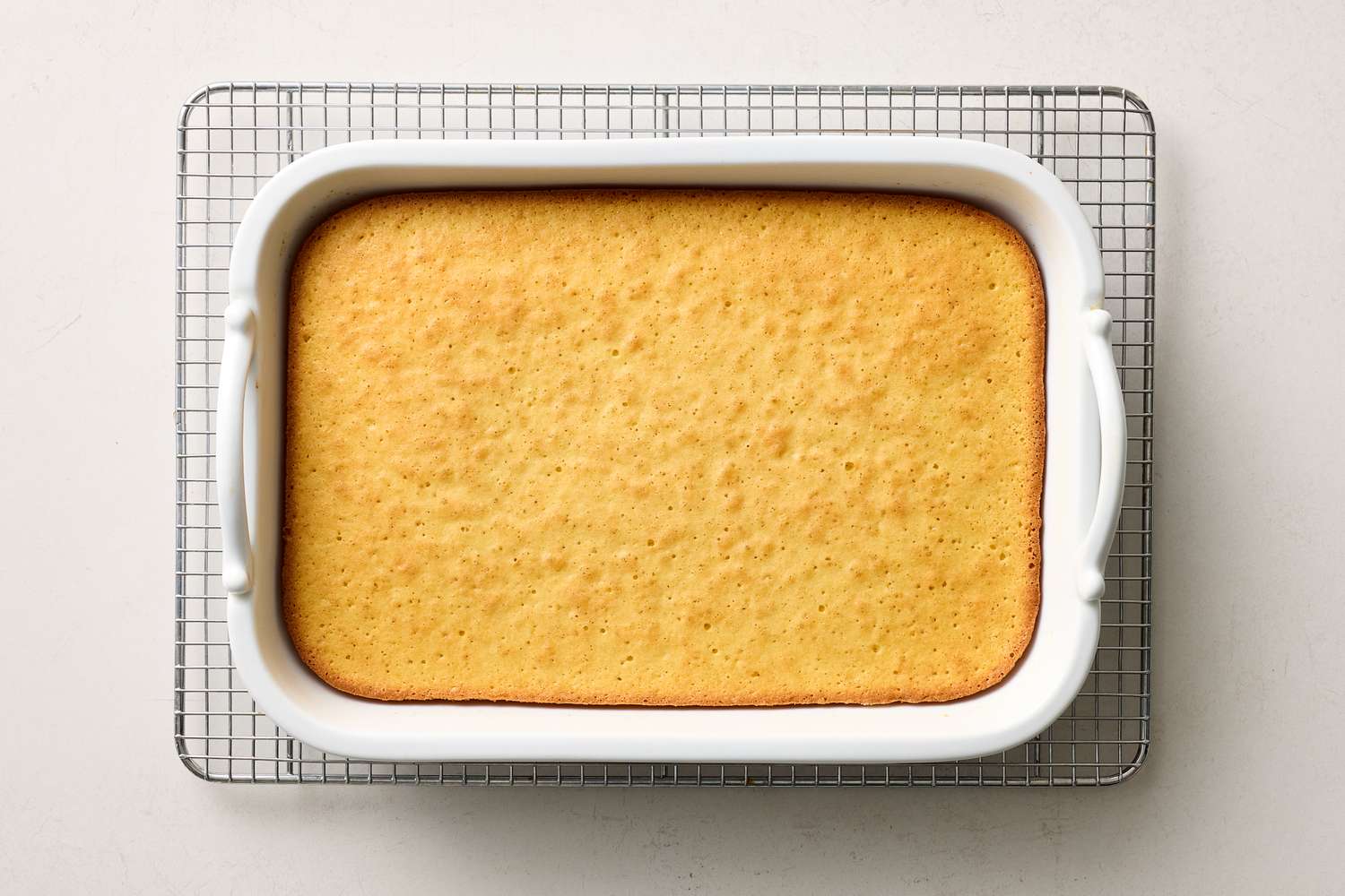 Baked tres leches cake in a rectangular white dish on a cooling rack