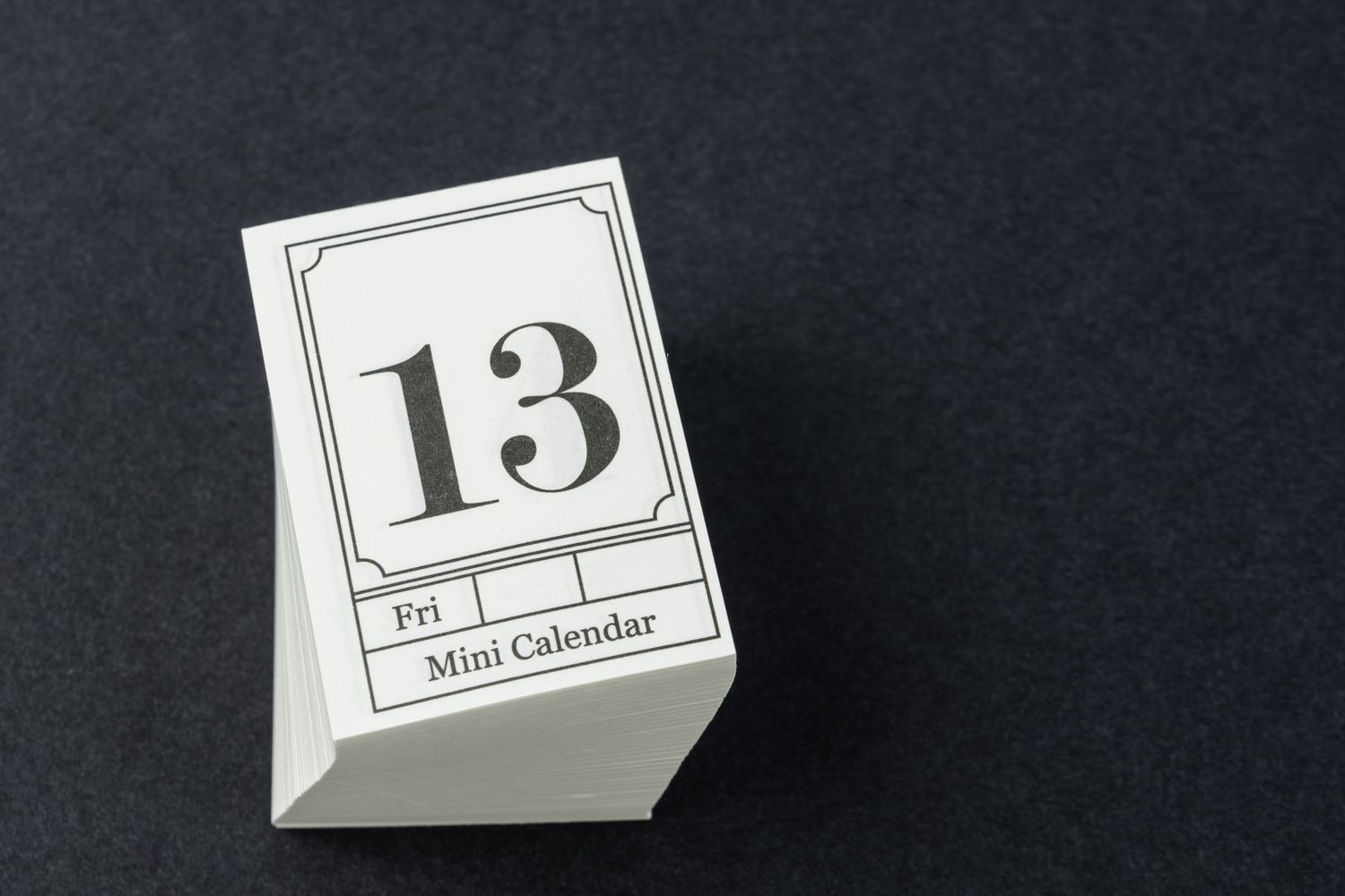 A mini desk calendar displaying the number 13 and the day Friday on a dark surface