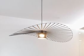 A modern ceiling light with a linear wave design suspended in a minimalist room