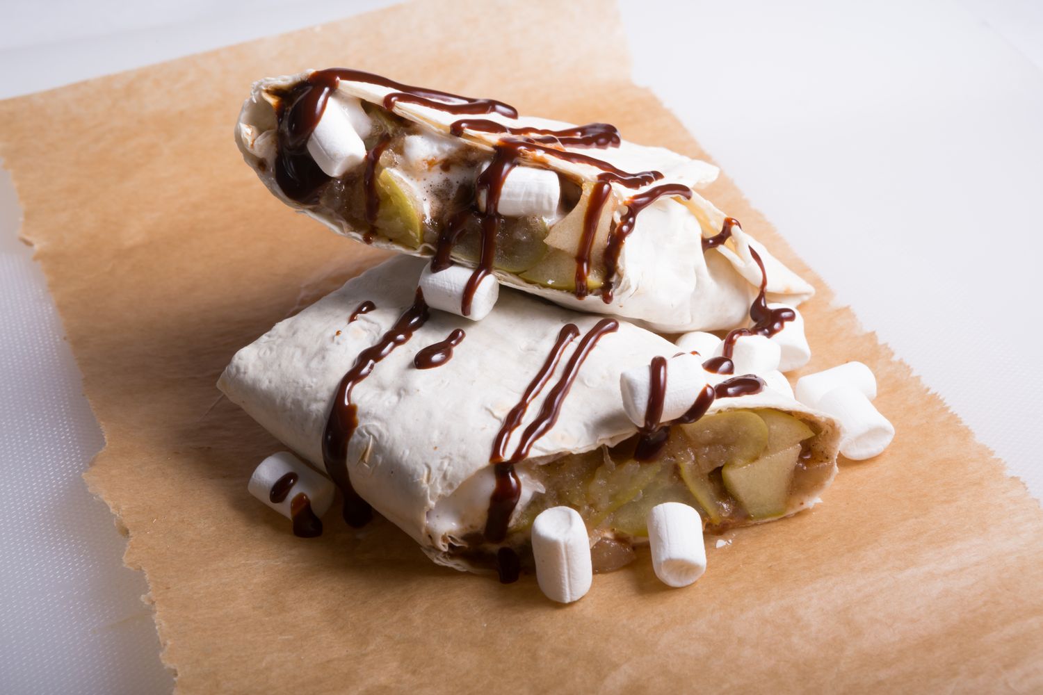 Dessert wraps filled with fruit topped with marshmallows and drizzled with chocolate