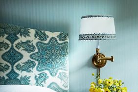 Blue striped wallpaper with golden wall sconce and paisley headboard