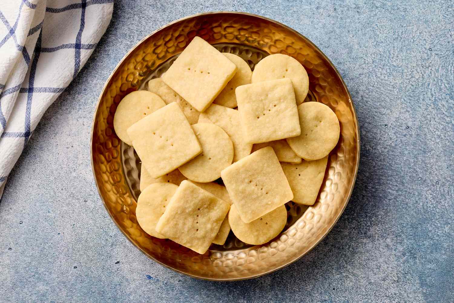 A bowl of rectangular and circular shortbread cookies on a textured blue surface