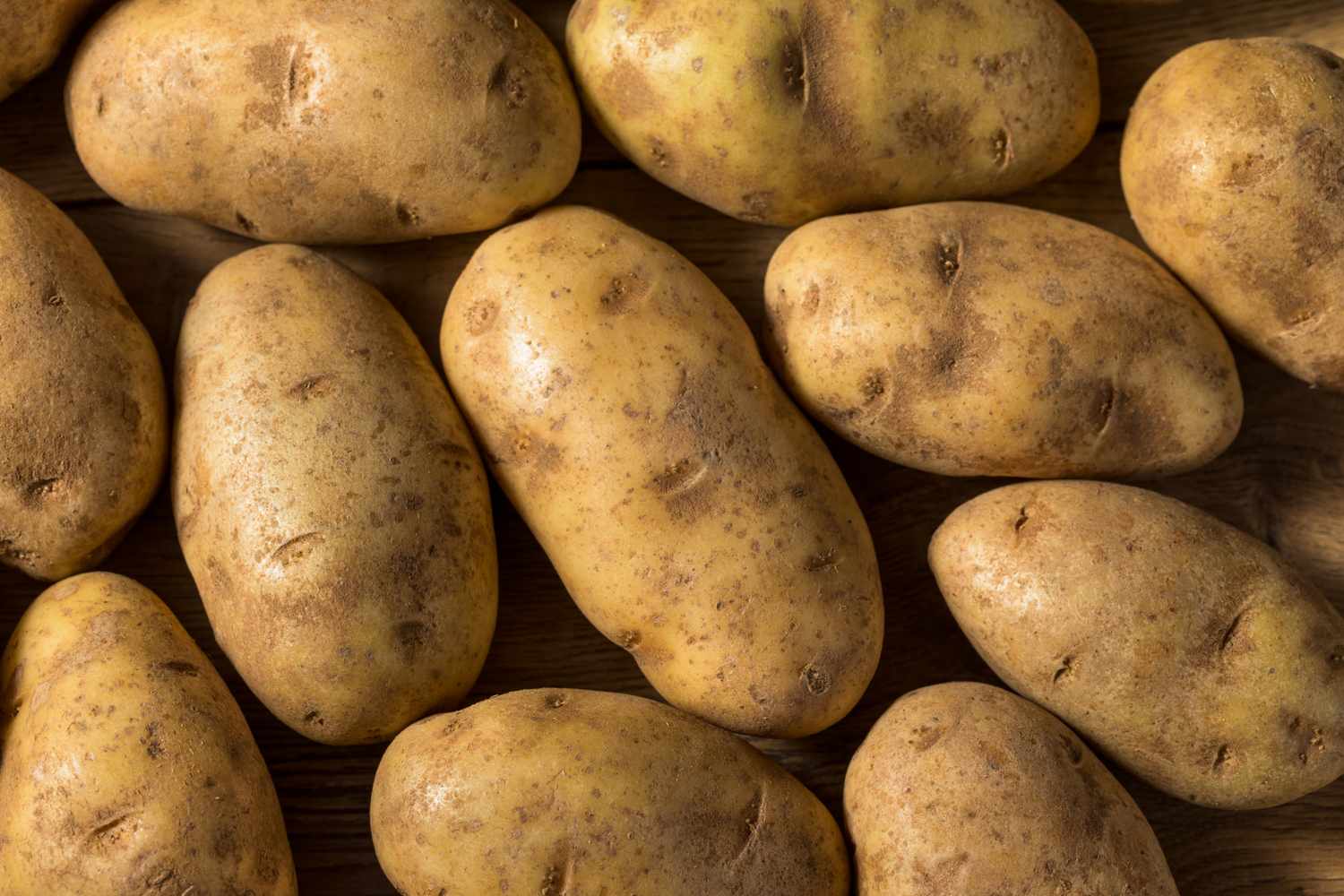 A collection of russet potatoes placed on a wooden surface