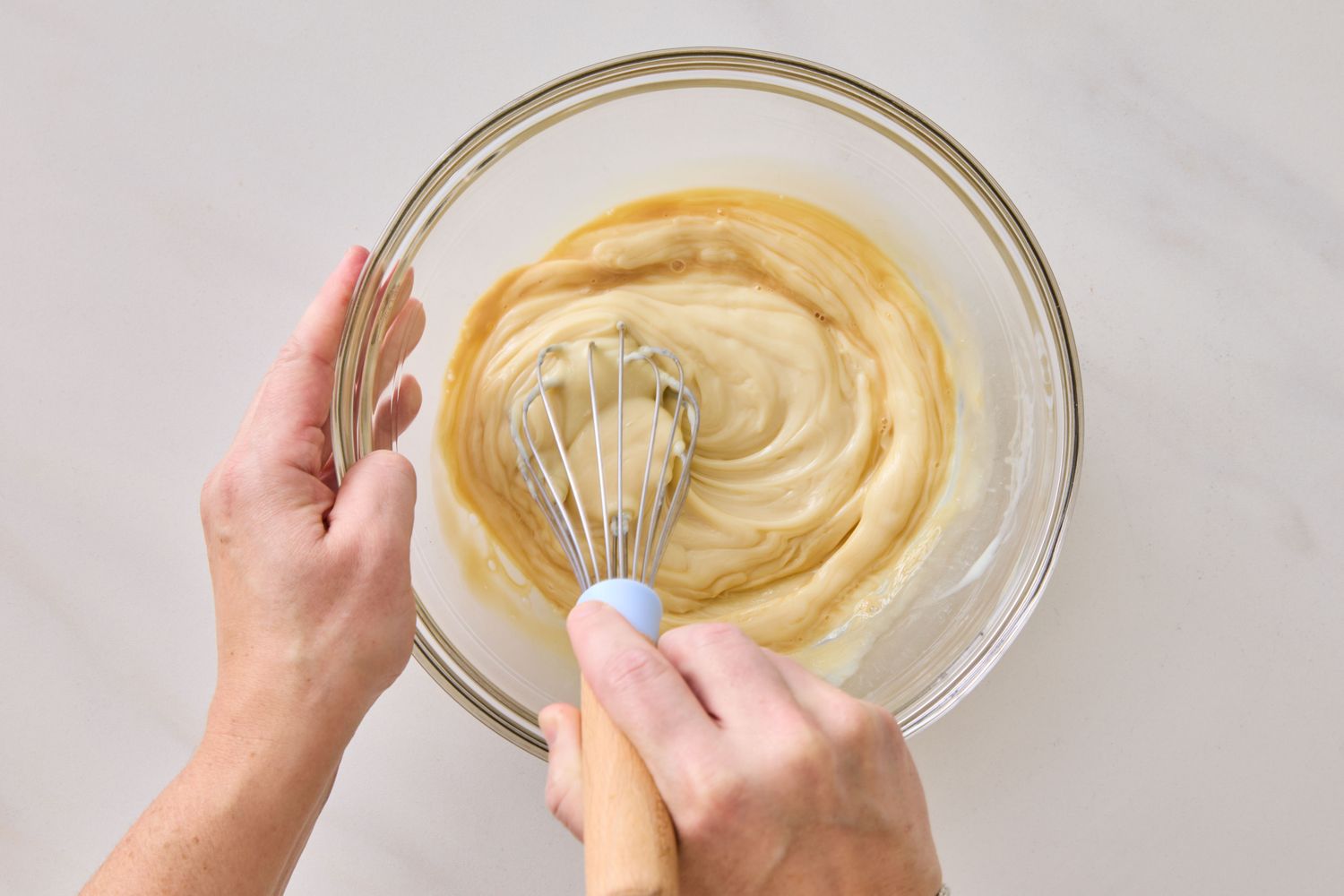 Hands whisking a mixture in a glass bowl
