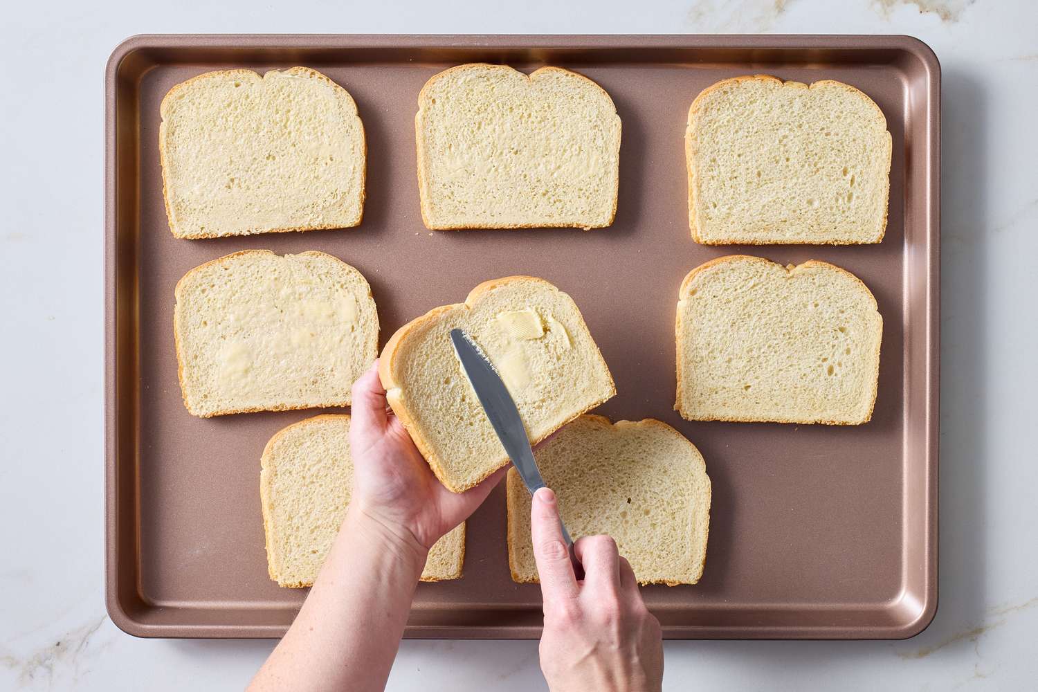 Sliced bread on a tray a hand spreading butter on a slice of bread with a knife