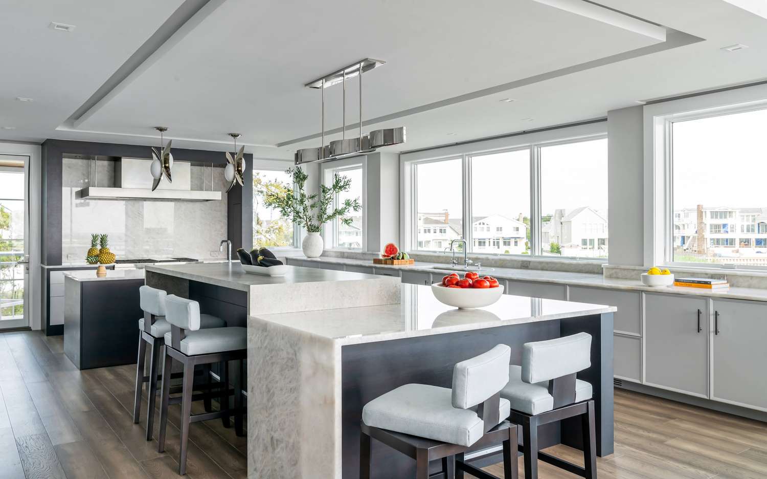Modern kitchen featuring a large island with stools a second smaller workspace preparation counter and ample natural lighting from large windows displaying decorative items