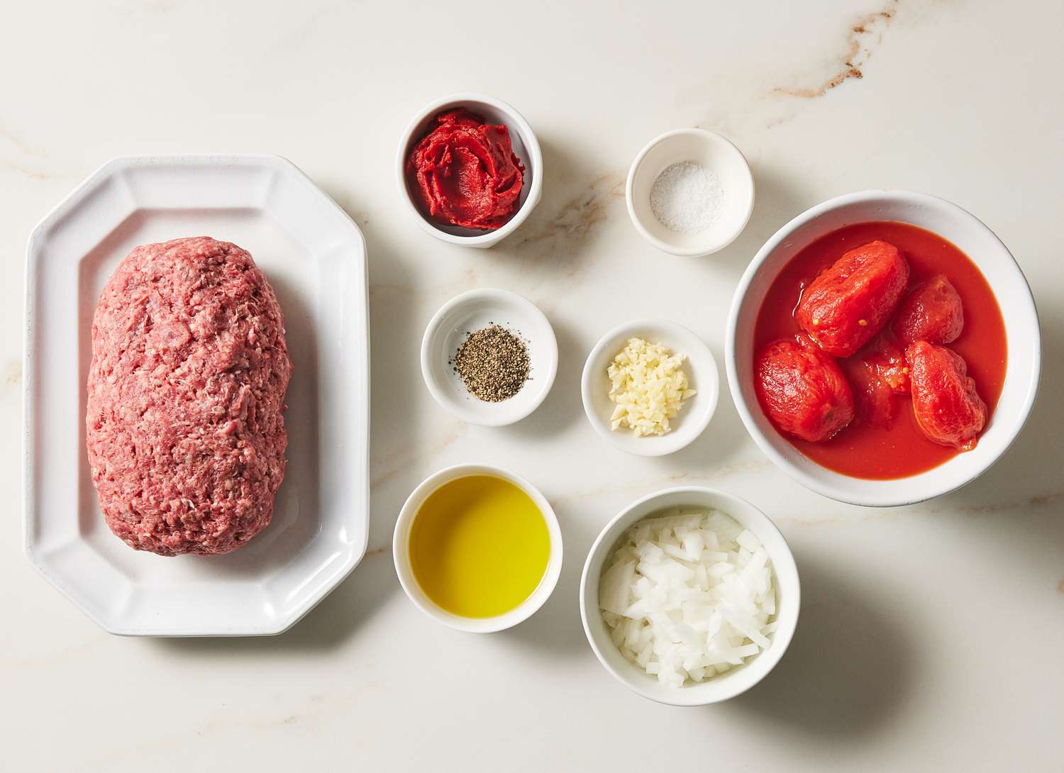 raw beef and bowls of ingredients on a marble surface