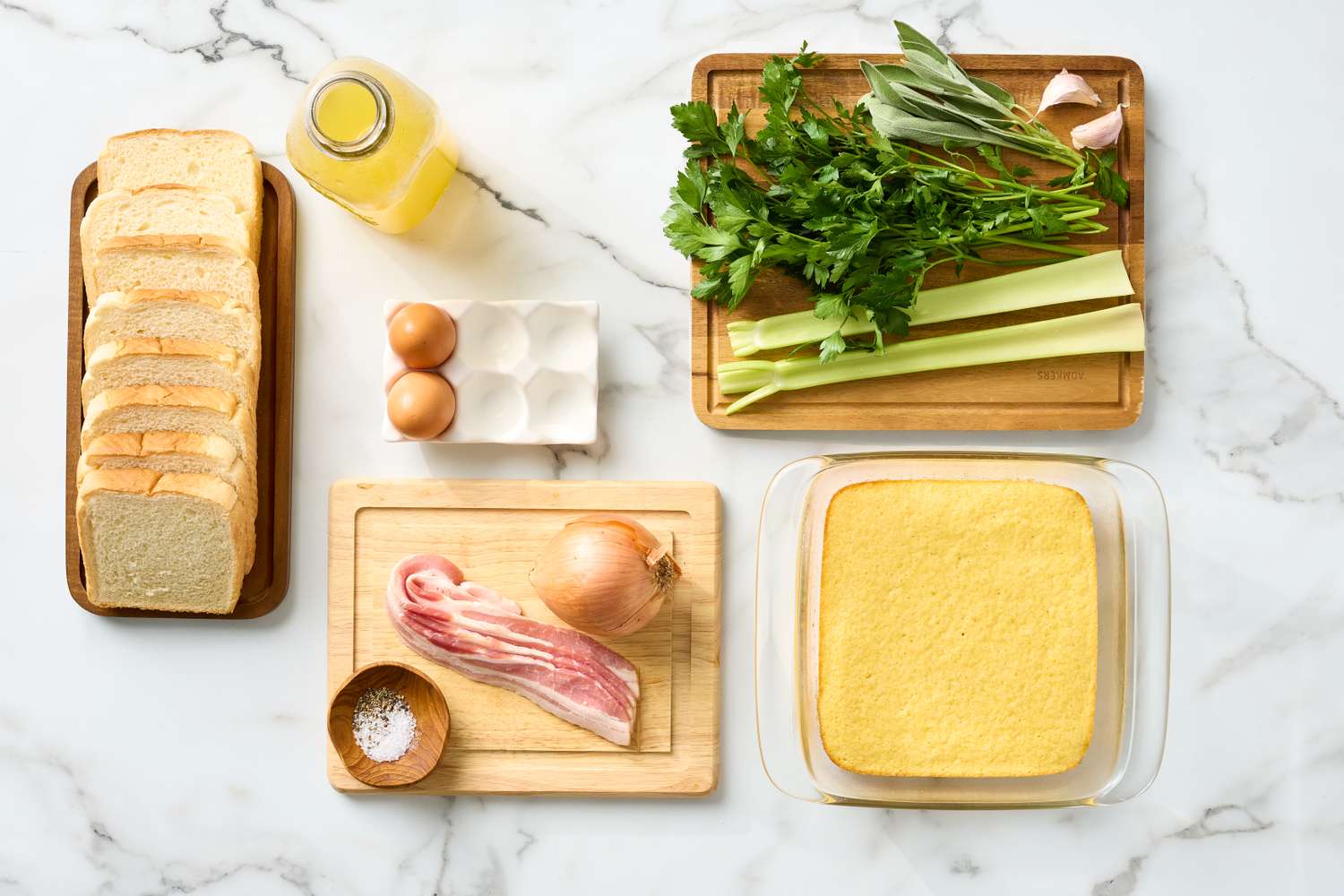 Ingredients for cornbread stuffing including bread cornbread bacon eggs herbs and vegetables arranged on a table