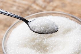 A spoon holding granulated sugar above a bowl of sugar