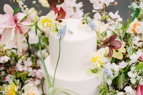two tiered white frosted wedding cake surrounded by floral display