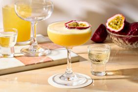 A passion fruit martini garnished with a passion fruit half, accompanied by a shot glass and additional cocktails in the background