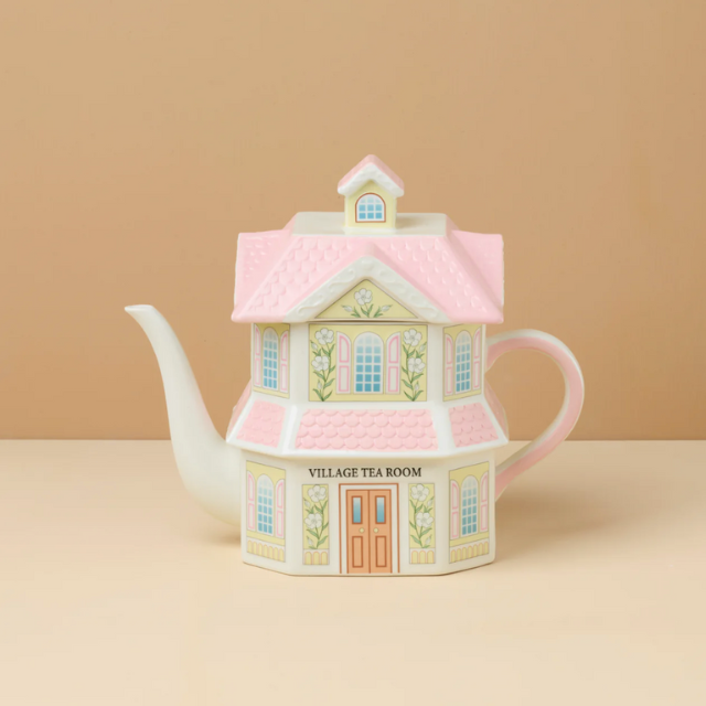 A teapot designed to resemble a house labeled Village Tea Room on a plain background