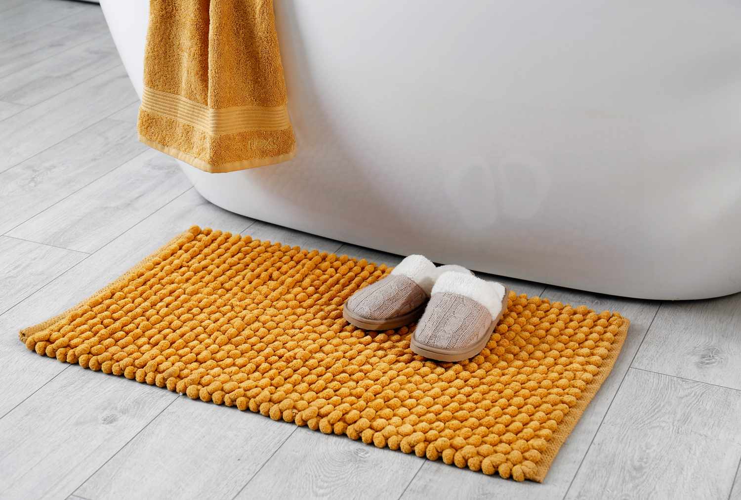 A soft bath mat and slippers placed near a bathtub