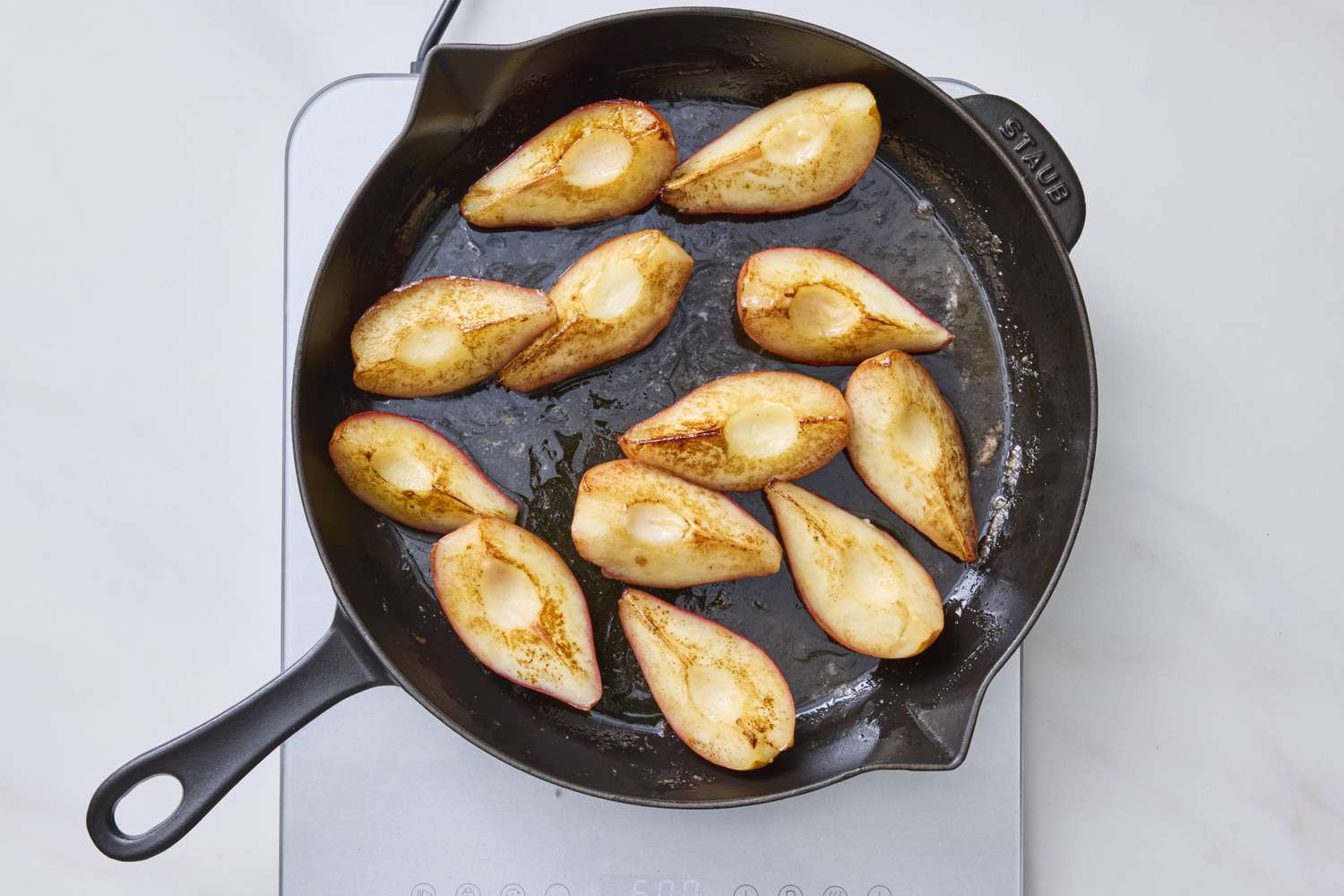 Caramelized pear halves in a skillet on a stovetop