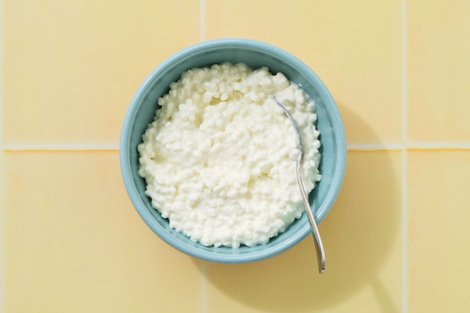 A bowl of cottage cheese with a spoon on a tiled surface