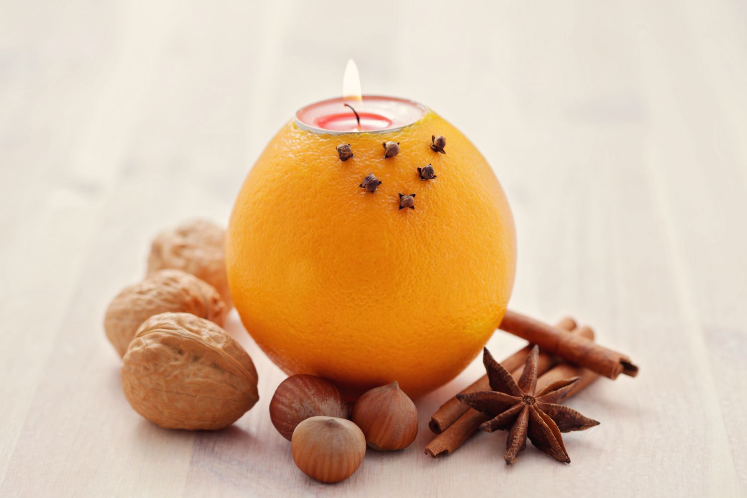 An orange with a candle inserted surrounded by spices and nuts