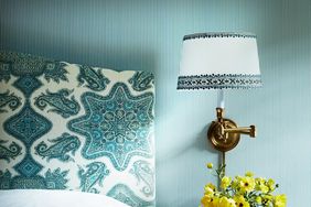 Blue striped wallpaper with golden wall sconce and paisley headboard