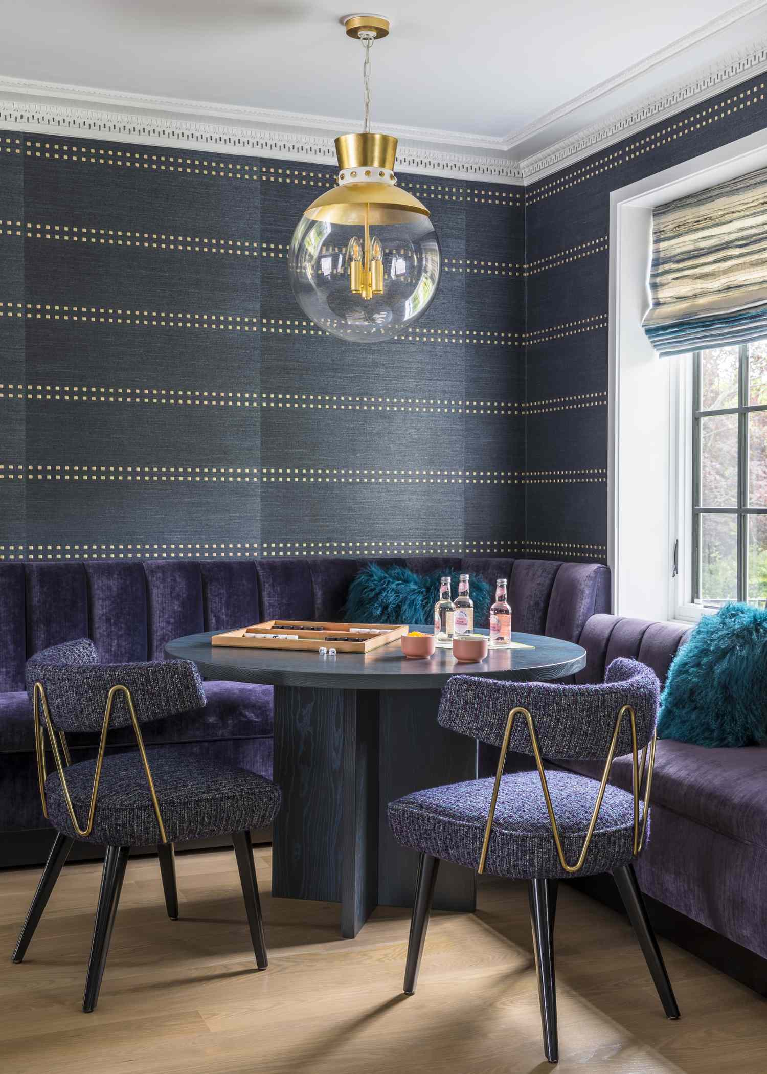 A dining nook with a round table chairs and a built in banquette seating near a window