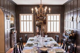A formal dining room with a set table chairs arranged and a chandelier hanging in the center of the room