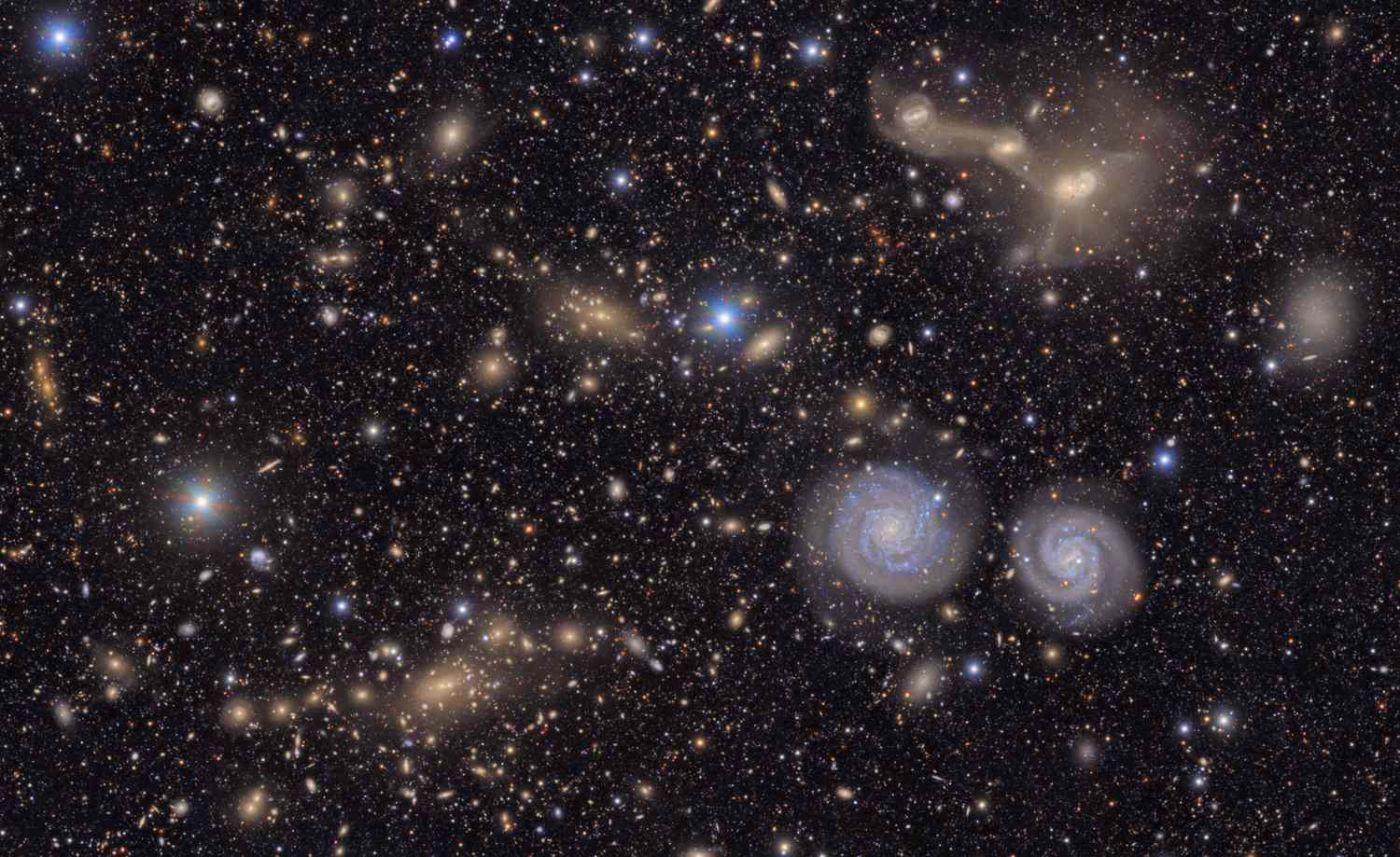 A distant view of galaxies and celestial objects in outer space, featuring prominent spiral galaxies and clusters of stars