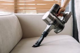 A hand uses a handheld vacuum on a sofa