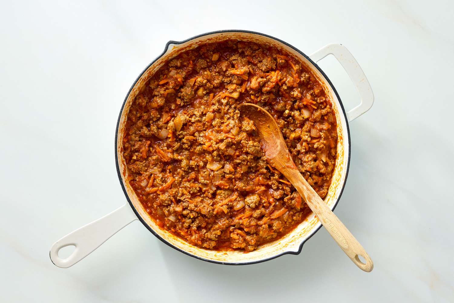 Casserole dish containing a cooked mixture of ground meat and rice with a wooden spoon resting inside