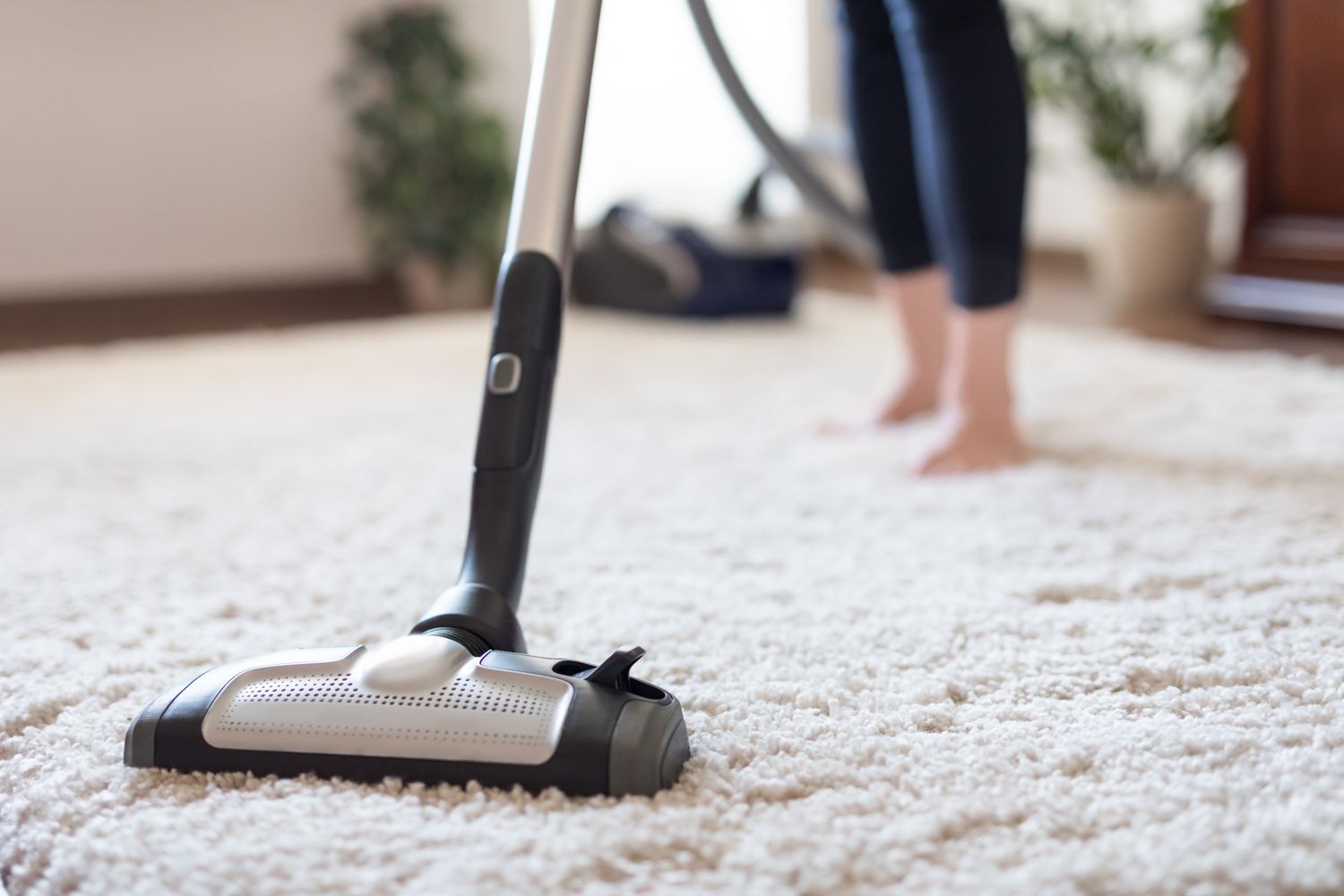Young woman using a vacuum cleaner while cleaning carpet in the house.