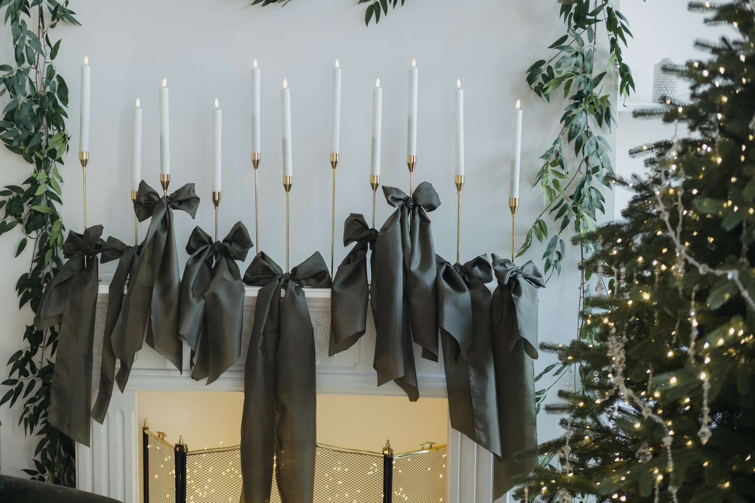 Decorative fireplace mantel with candles large bows and garlands beside a decorated Christmas tree