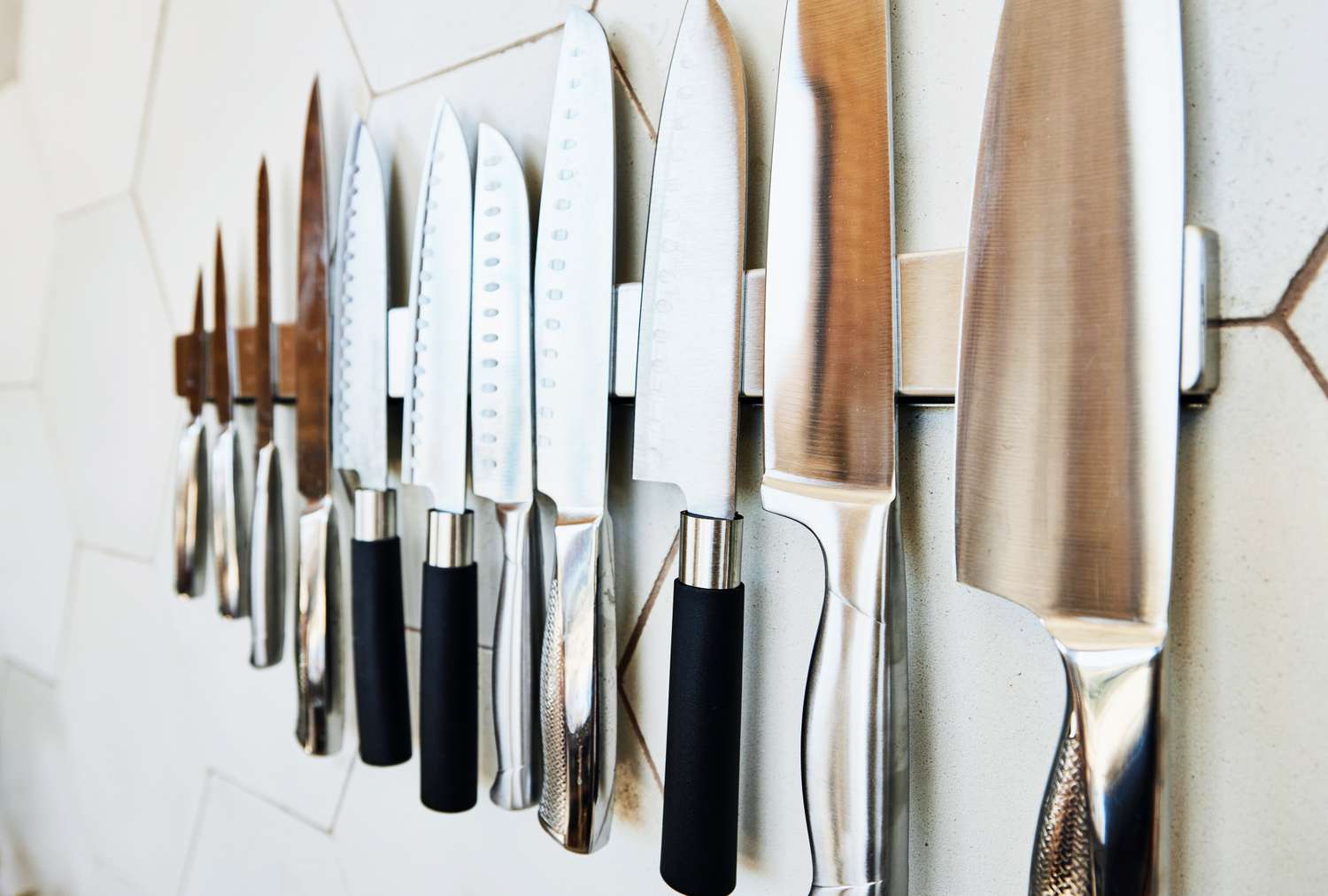 A magnetic knife holder mounted on a tiled wall holds various kitchen knives displayed in a row