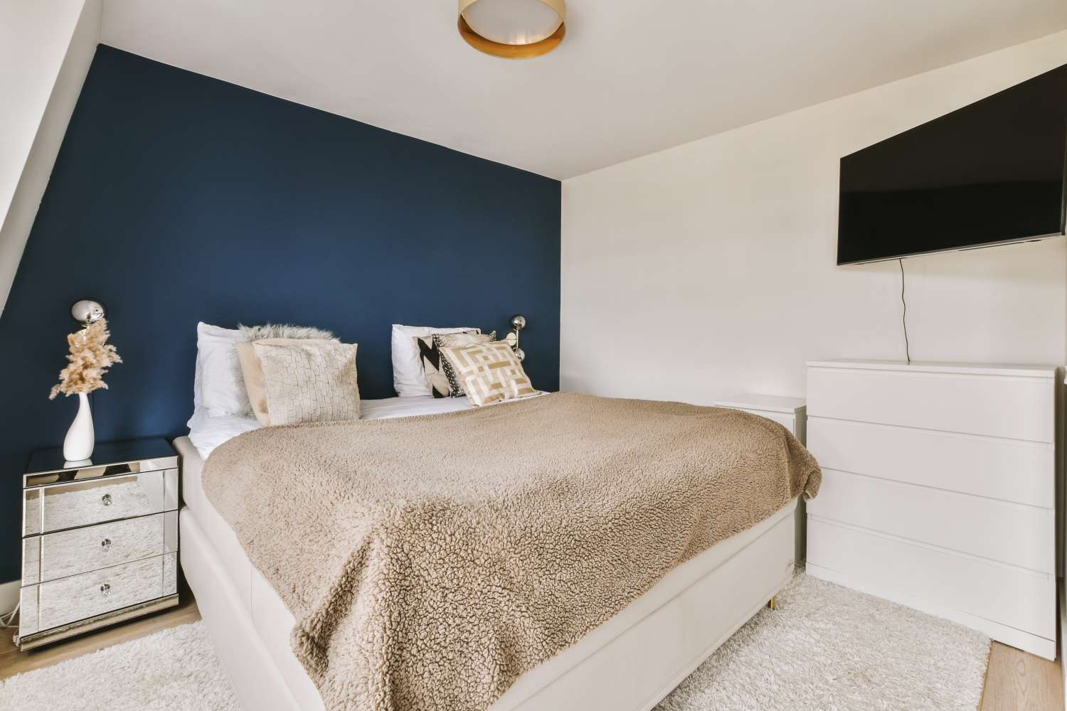 A modern bedroom with a bed dresser TV and a navy blue accent wall