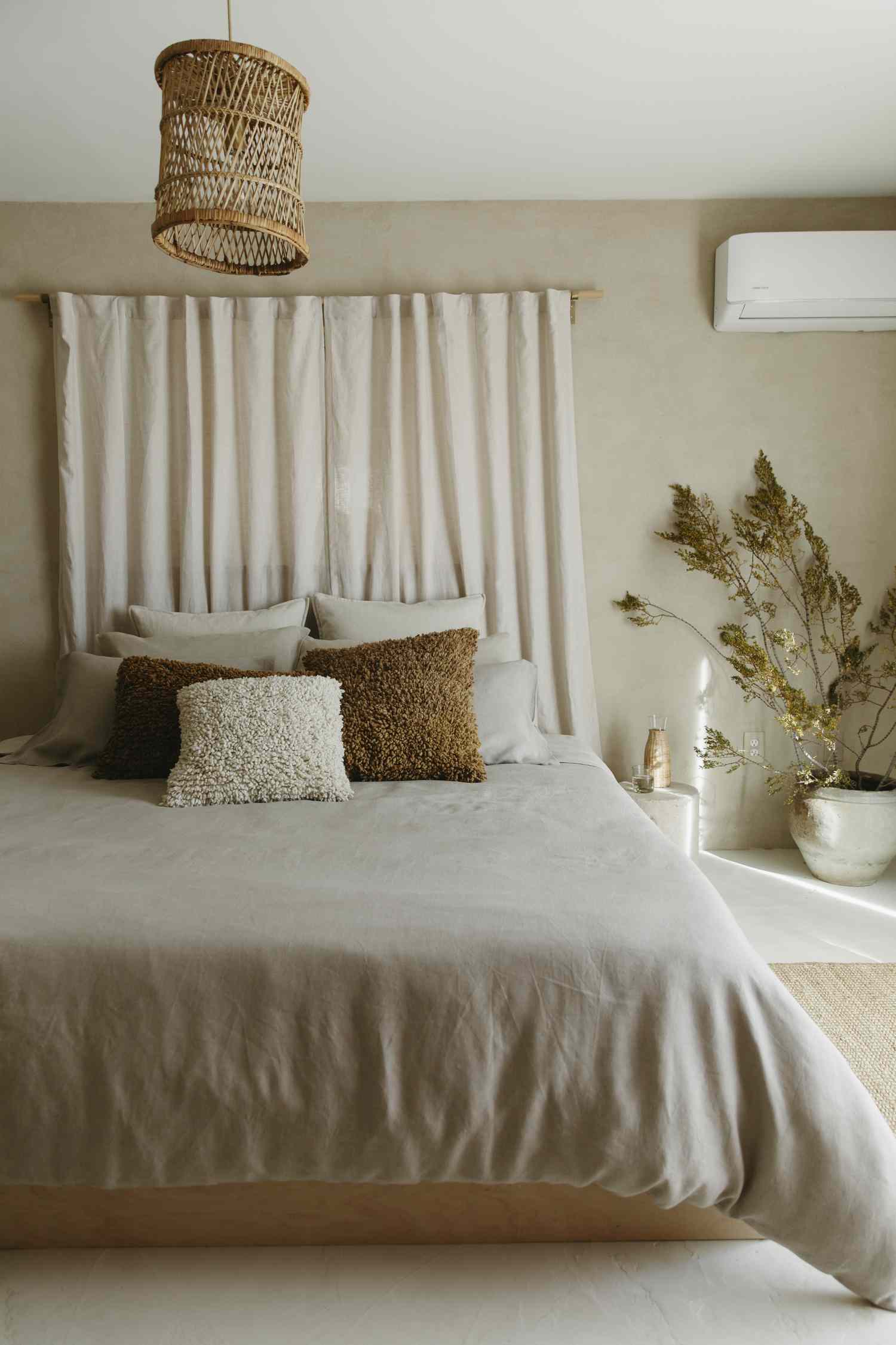 A neatly arranged bedroom with a beige bed decorative pillows hanging light fixture and indoor potted plant